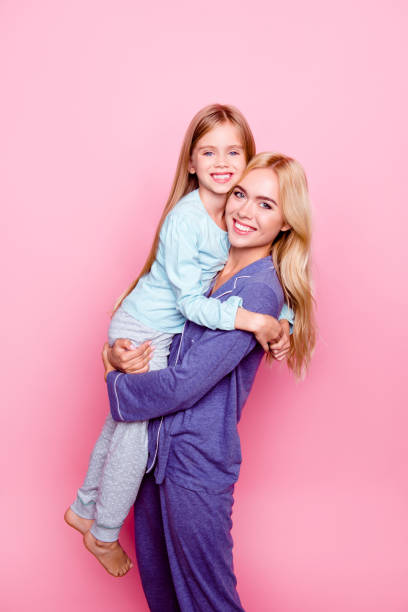 concept of kindness, happiness and spending time together with a family. goodnight! mother and her little daughter clothed in pajamas get ready for going to bed, isolated on pink background - blond hair carrying little girls small imagens e fotografias de stock