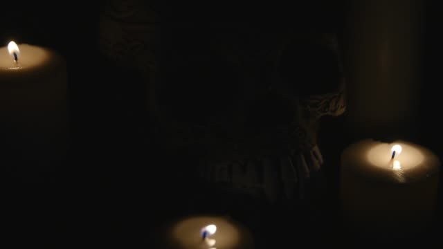 four lighted candles and a skull on a black background. close up
