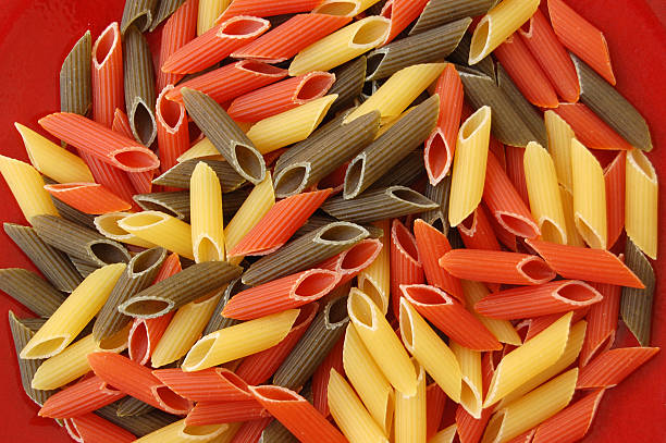 makaron penne tricolore na czerwonym tle - penne rigatoni pasta tomato pasta zdjęcia i obrazy z banku zdjęć