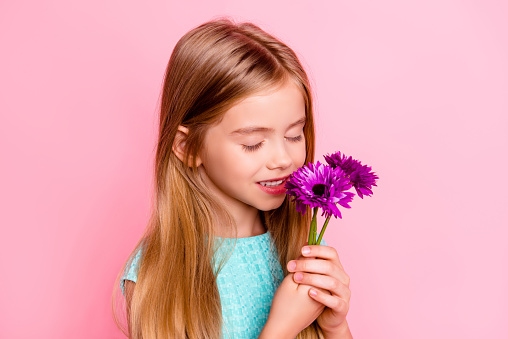 Close up portrait of happy cute lovely beautiful tender gentle girl with toothy smile, she is smelling flowers in hands with closed eyes, isolated on bright pink background