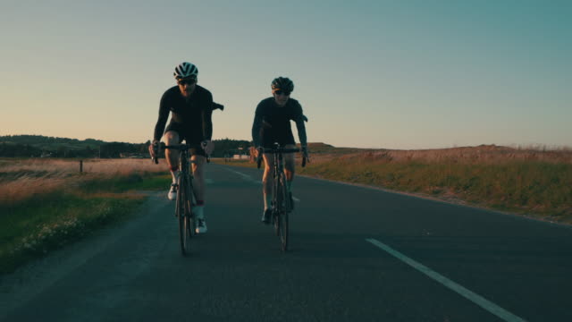 2 cyclists riding country roads at sunset