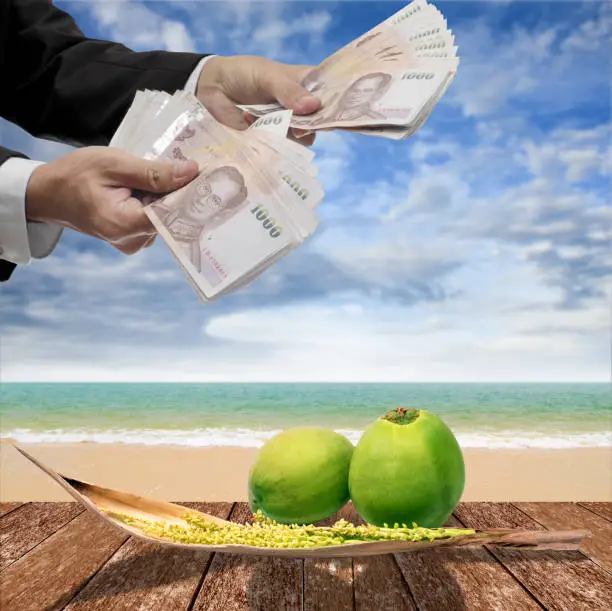 Photo of Businessman pay for coconut and spadix flower of coconut on deck and sea background