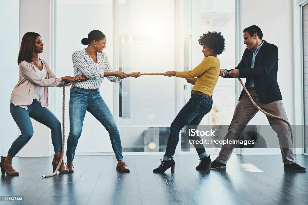 It's a competitive market out there with many challenges Shot of a group of businesspeople pulling on a rope during tug of war in an office Competition Stock Photo