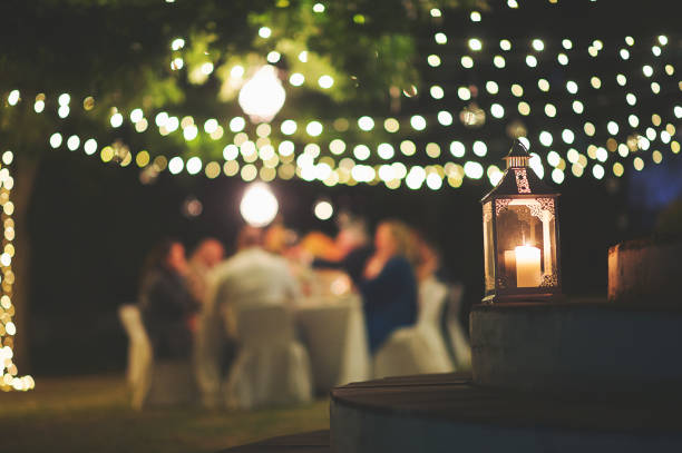 Candle and string lights outdoor dinner A string of fairy lights and a chandelier with candle hanging in-between trees photographed shining at night with image focus technique focus on the foreground bokeh background and dark and a table with peopleFranschhoek Cape Winelands South Africa people banque stock pictures, royalty-free photos & images