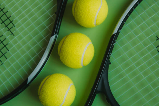 istock Three tennis balls and two rackets on green background. 926574180