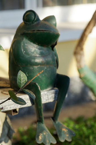 Steel green frog sits in crossed legs gesture on stone stairs. Garden statue Selective focus on the face of frog