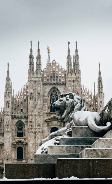 Falling snowflakes at ornate of lion on Piazza del Duomo in Milan, Lombardy, Italy. The Patron Saint of Milan, Madonnina, is visible above the Duomo Cathedral, with copy space stock photo