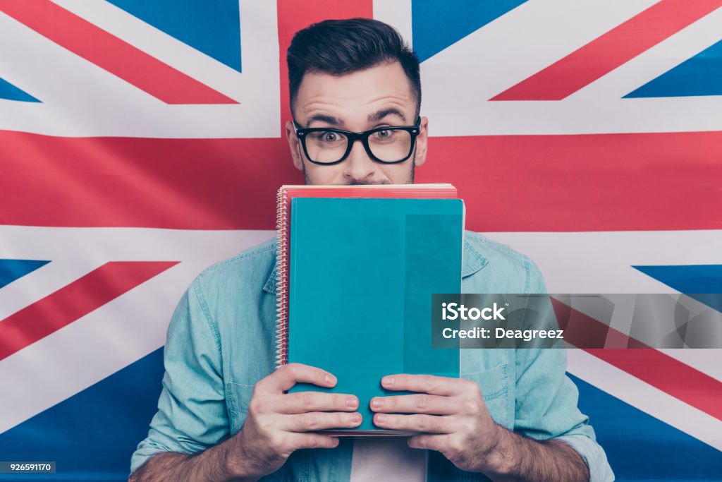 Langue anglaise concept-portrait d’un homme heureux holding coloré copie d’apprentissage livres en mains visage moitié de clôture avec les ordinateurs portables permanent sur fond de drapeau anglais - Photo de Langue anglaise libre de droits