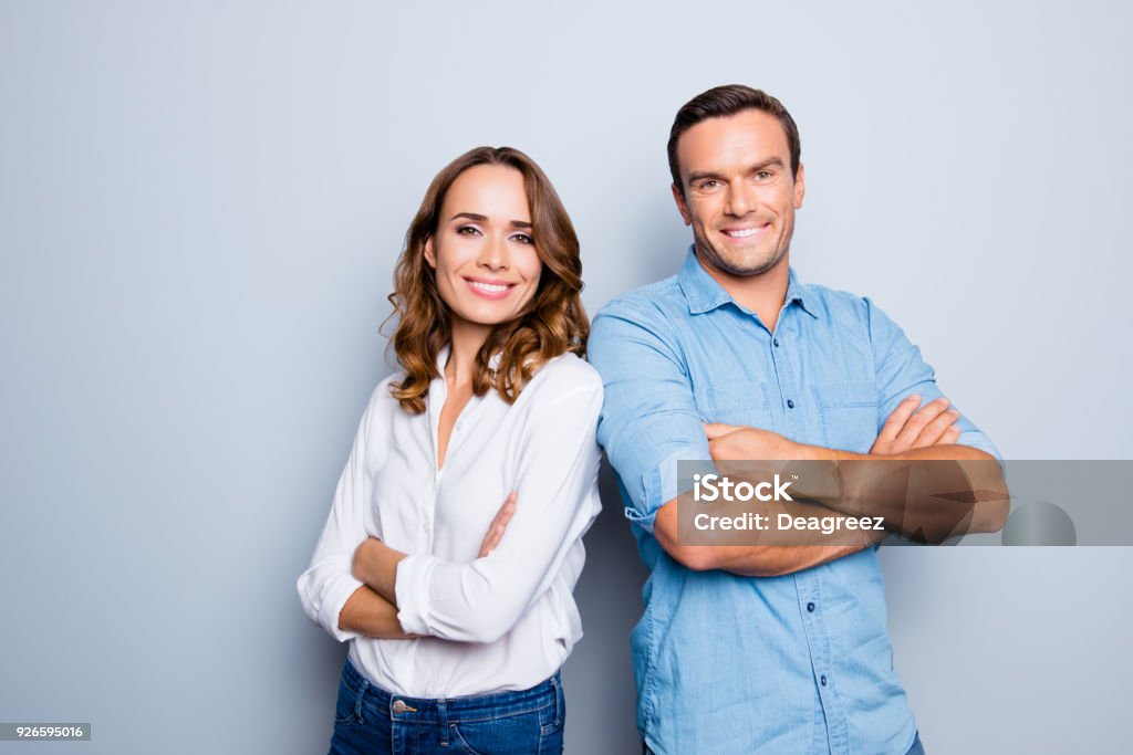 He vs she happy together. Close up portrait of attractive, caucasian, lovely, cute, adult couple in casual outfit  looking at camera standing with crossed arms over grey background Women Stock Photo
