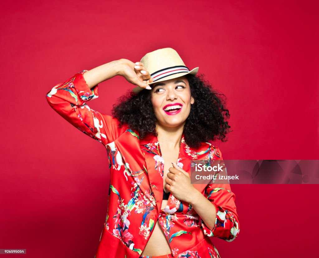 Summer portrait of excited young woman against red background Summer portrait of beautiful, excited young woman wearing red floral pattern jacket and sunhat, standing against red background. 20-24 Years Stock Photo