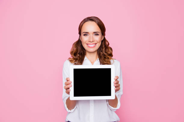 Beautiful charming smiling happy woman with beaming smile is showing a tablet with empty black screen, isolated on bright pink background