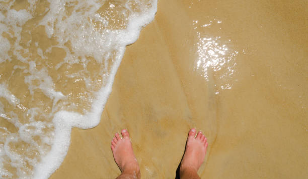 istock feet on wet beach sand and small wave with white foam coming in. 926598010