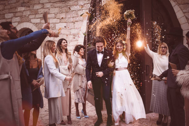 newlywed couple walking out church and celebrating wedding with confetti - throwing people stone tossing imagens e fotografias de stock