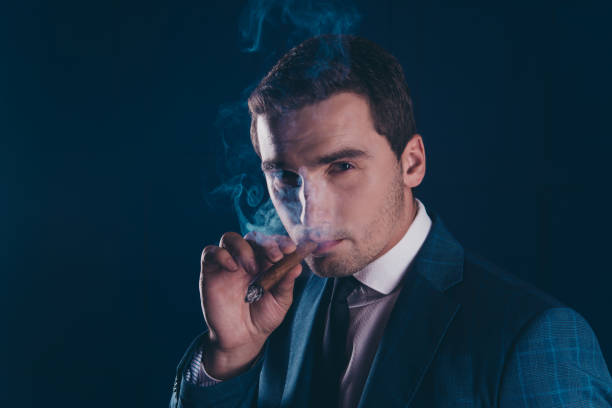 fechar o retrato de charuto fumar de homem atraente, elegante, elegante, deslumbrante sobre fundo azul escuro - nicotine healthcare and medicine smoking issues lifestyles - fotografias e filmes do acervo