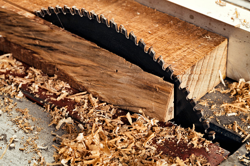 Male carpenter using saw in home workshop with wood chips flying