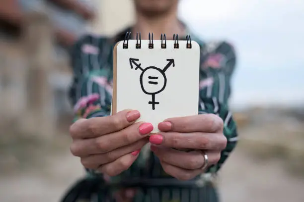 closeup of a young caucasian woman outdoors showing a notepad in front of her with a transgender symbol drawn in it