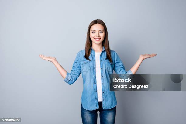 Portrait Of Successful Cheerful Cute Young Woman Presenting Something Showing Copy Space On Her Palm In Two Sides Looking At Camera Standing Over Grey Background Stock Photo - Download Image Now