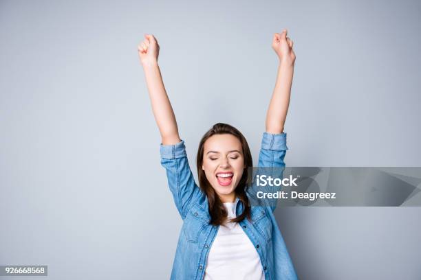 Amazed Brunette Young Business Woman In Casual Shirt Is Gesturing Victory With Her Raised Hands She Is Shocked Extremely Happy With Closed Eyes Beaming Smile Open Mouth On Grey Background Stock Photo - Download Image Now