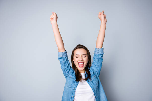 mulher de negócios jovem morena espantado em camisa casual é vitória de gestos com as mãos levantadas, ela é chocado, extremamente feliz, com os olhos fechados, radiante sorriso, boca aberta com fundo cinza - university education screaming shouting - fotografias e filmes do acervo