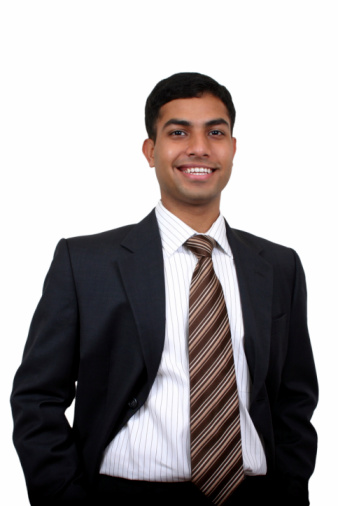 Portrait of Indian young businessman in suit smiling at camera while walking along the office corridor to the work