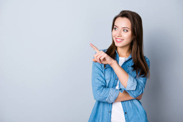 концепция рекламы. успешная женщина-кавказ с сияющей улыбкой на сером фоне указывает указательным пальцем и смотрит на пустое пространств� - business pointing women index finger стоковые фото и изображения