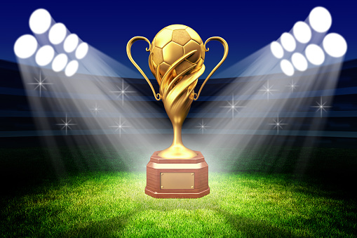 Football winner cup with a golden soccer ball in the light of spotlights on the green grass field of the stadium