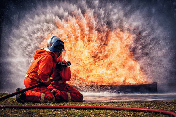 Firefighter in fire fighting suit spraying water, Firemen fighting  raging fire with huge flames of burning, Fire prevention and extinguishing concept