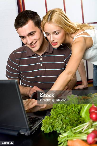 Photo libre de droit de Jeunes Heureux Souriant Couple Attrayant Cuisine Dans La Cuisine Avec Ordinateur Portable banque d'images et plus d'images libres de droit de Adulte