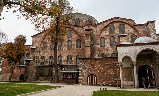 Istanbul, Turkey - November 16, 2017:  Exterior view, showing a man walking through the Ottoman style, arched and domed entrance of the stone and brick built Aya Irini (Hagia Irene), a former Greek Eastern Orthodox church, now used as a museum and concert hall, located in the outer courtyard of Topkapi Palace in Istanbul, Turkey, November 16, 2017
