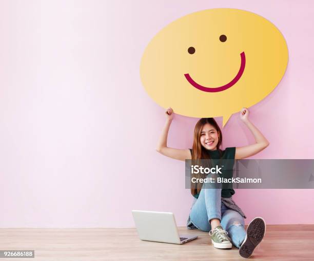 Photo libre de droit de Concept De Client Heureux Lexamen Et La Rétroaction Son Expérience Pour Lenquête De Satisfaction En Ligne Jeune Femme En Posture Gai Suscite Une Bulle De Dialogue Avec Smiley Face Assis Sur Le Sol Avec Ordinateur Portable banque d'images et plus d'images libres de droit de Client