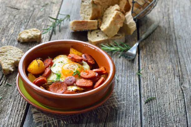 Spanish tapa: Spicy chorizo sausage with fried egg and baby potatoes served in a terra cotta cazuela dish