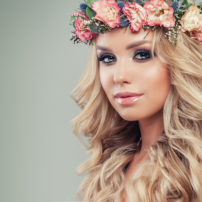 Beautiful Female Face. Nice Young Woman with Makeup, Flowers, Blonde Wavy Hair. Skincare and Haircare Concept