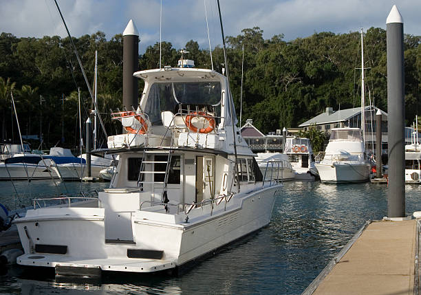 Port Douglas, Queensland, Australia - July 29, 2025: Small boat moving through still waters, surrounded by yachts, palm trees, and distant hills at the Port Douglas marina in Queensland, Australia
