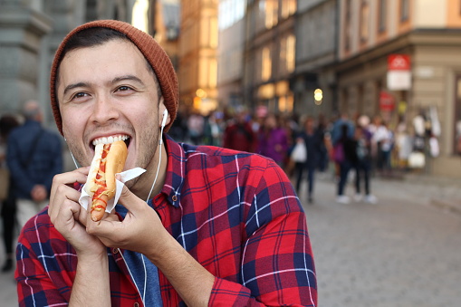 Ethnic male devouring a hot dog.
