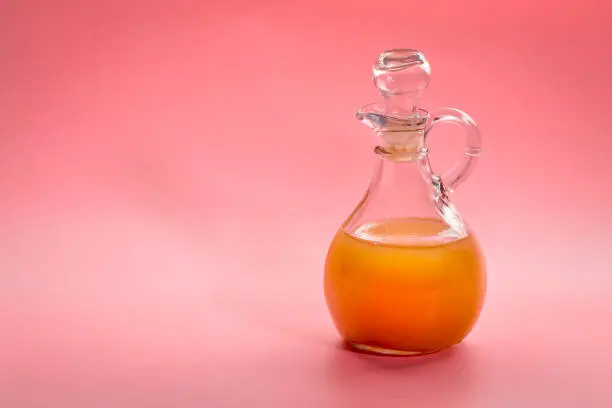 unfiltered, raw apple cider vinegar with mother - a glass cruet against pink background