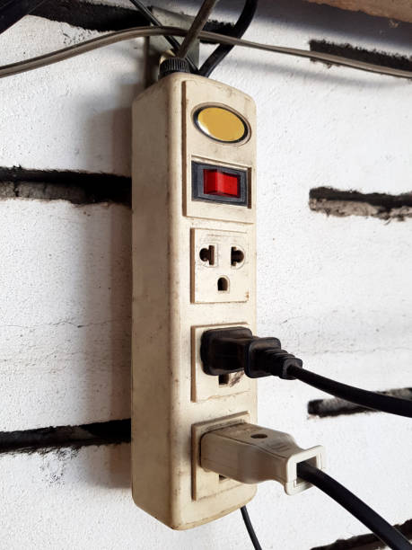 istock Two electrical cords connected to old white power strip or extension block, adapter plug electric charged with outlet socket plug on wall ,electric safety concept. 926703782