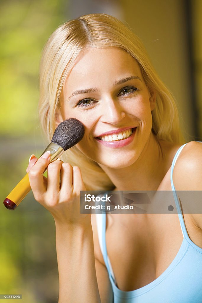 Portrait of smiling beautiful young woman with makeup brush indoors  Adult Stock Photo