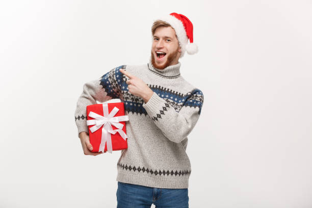istock Holiday Concept - Young beard man in sweater holding box and pointing hand on side. 926715016