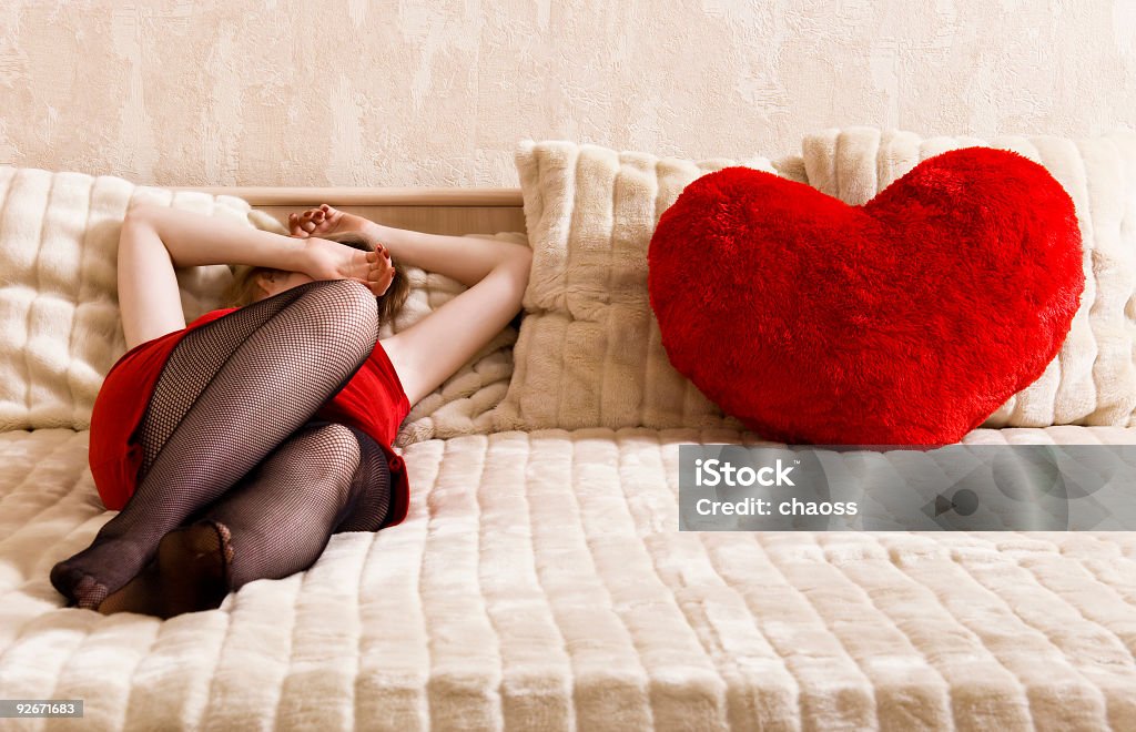 Młoda kobieta odpoczynku na łóżku i serce kształt poduszki - Zbiór zdjęć royalty-free (20-29 lat)