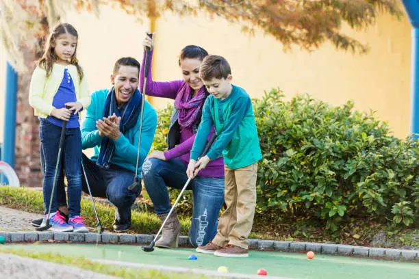 Interracial family with two children playing miniature golf together. The boy is 6 years old and his sister is 7. They are mixed race Hispanic and Caucasian.