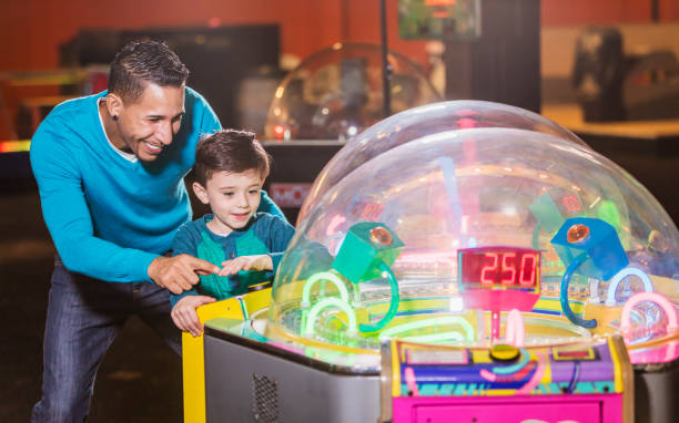 A father and his 6 year old son playing a game in an amusement arcade. They are mixed race Hispanic and Caucasian.