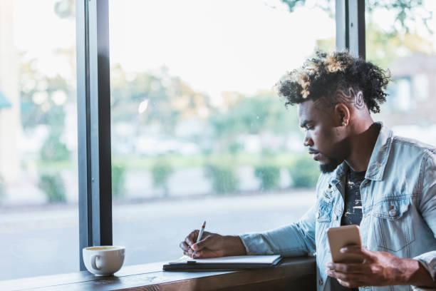 istock Mixed race man sitting by window in coffee shop, writing 926729810