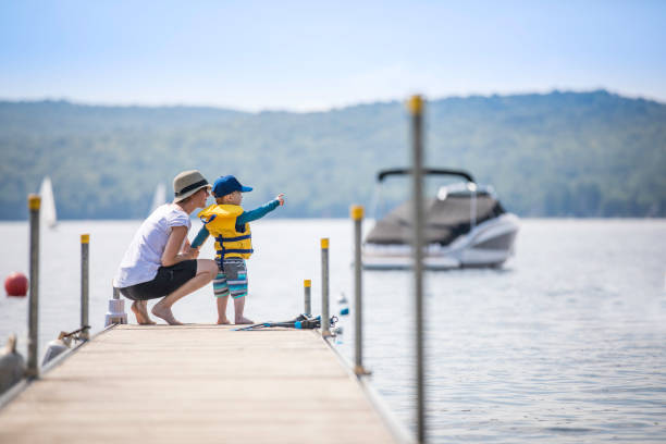 Mother and Son Looking at the View on Pier in Summer Mother and Son Looking at the View on Pier in Summer, there are boat and sailing boat in the background. Taken in Lac St-Joseph, Quebec, Canada life jacket stock pictures, royalty-free photos & images