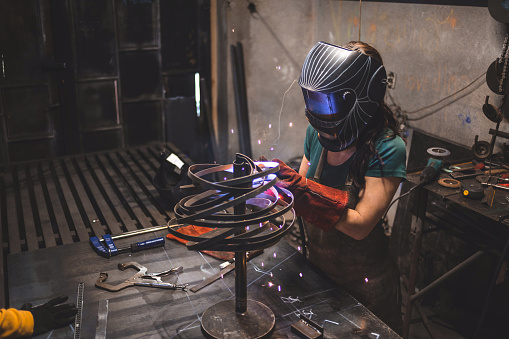 Gorgeous young girl designing a sculpture of metal, and making it.