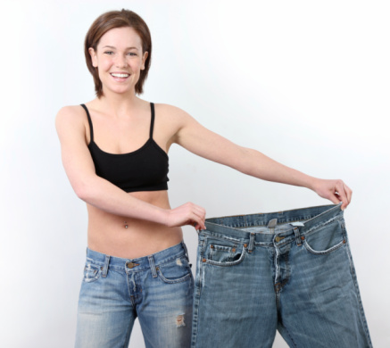 Happy young woman showing how much weight she lost by holding up an oversized pair of jeans