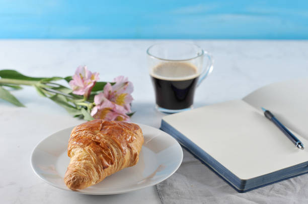 istock Open notebook with flowers and black coffee and croissant 926788860