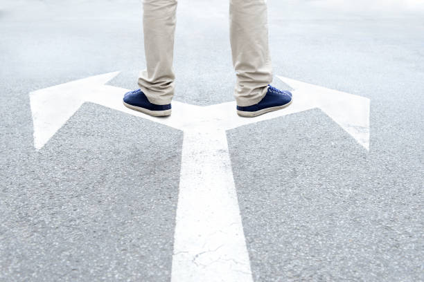 istock Young adult standing on arrows to make decision 926803084