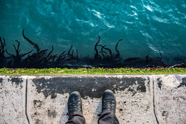 Subjective perspective of dark shoes and blue-green water at a water side from above in Venice.