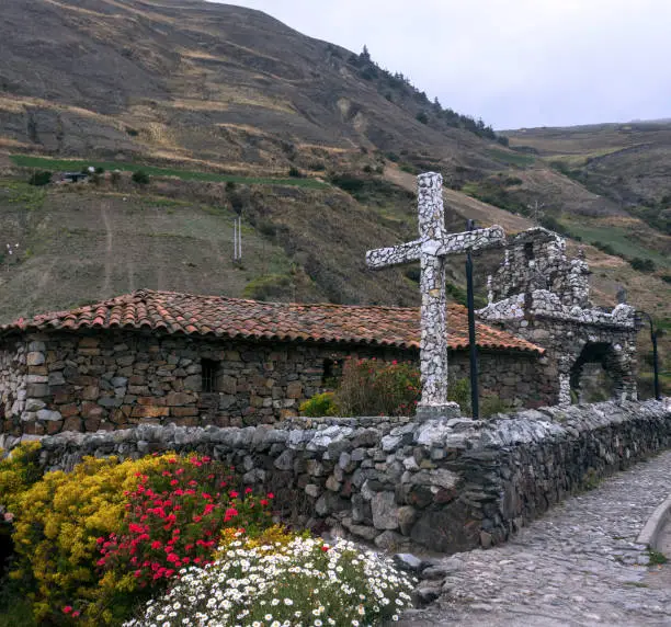 Stone cross surrounded by flowers of the garden, mountains and peaks of the Venezuelan Andes. 