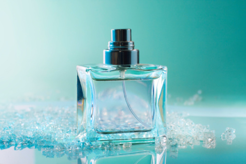A bottle of black glass with a perfume spray on a wavy blue background. Selective focus.